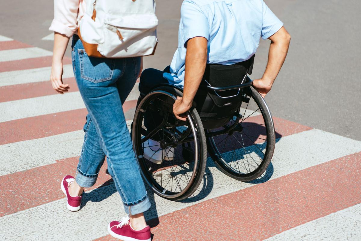 disabled man in wheelchair and woman crossing crosswalk in city