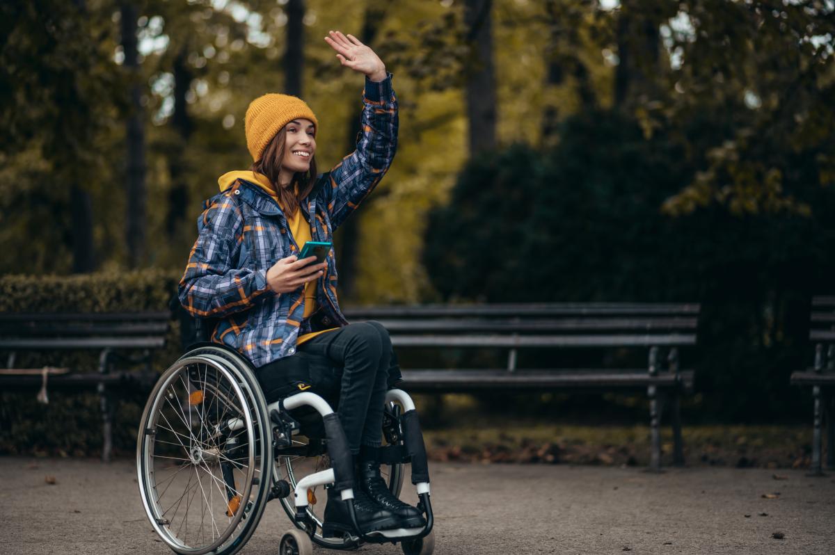 woman in a wheelchair waving to a friend while outside in a park