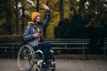 woman in a wheelchair waving to a friend while outside in a park